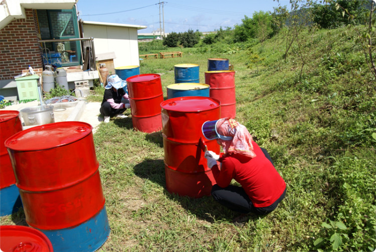 하천에 만들어질 배에 사용될 기름통에 색을 입히고 있습니다. 